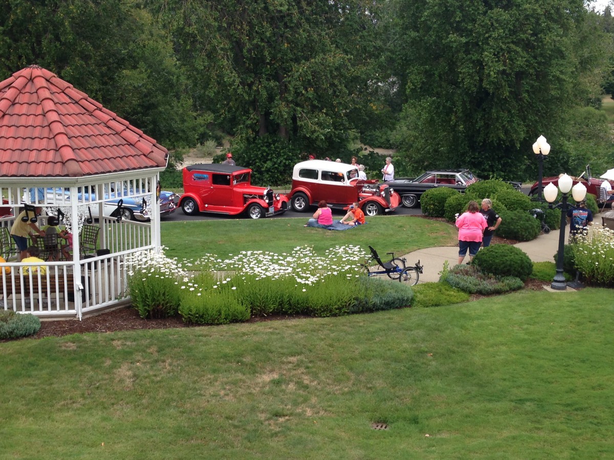 A park scene featuring classic cars on display near a gazebo, with people enjoying the summer event.