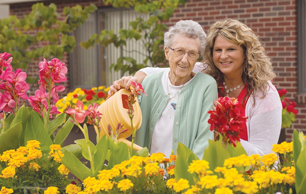 An older woman and a younger woman enjoying time in the garden, tending to colorful flowers.