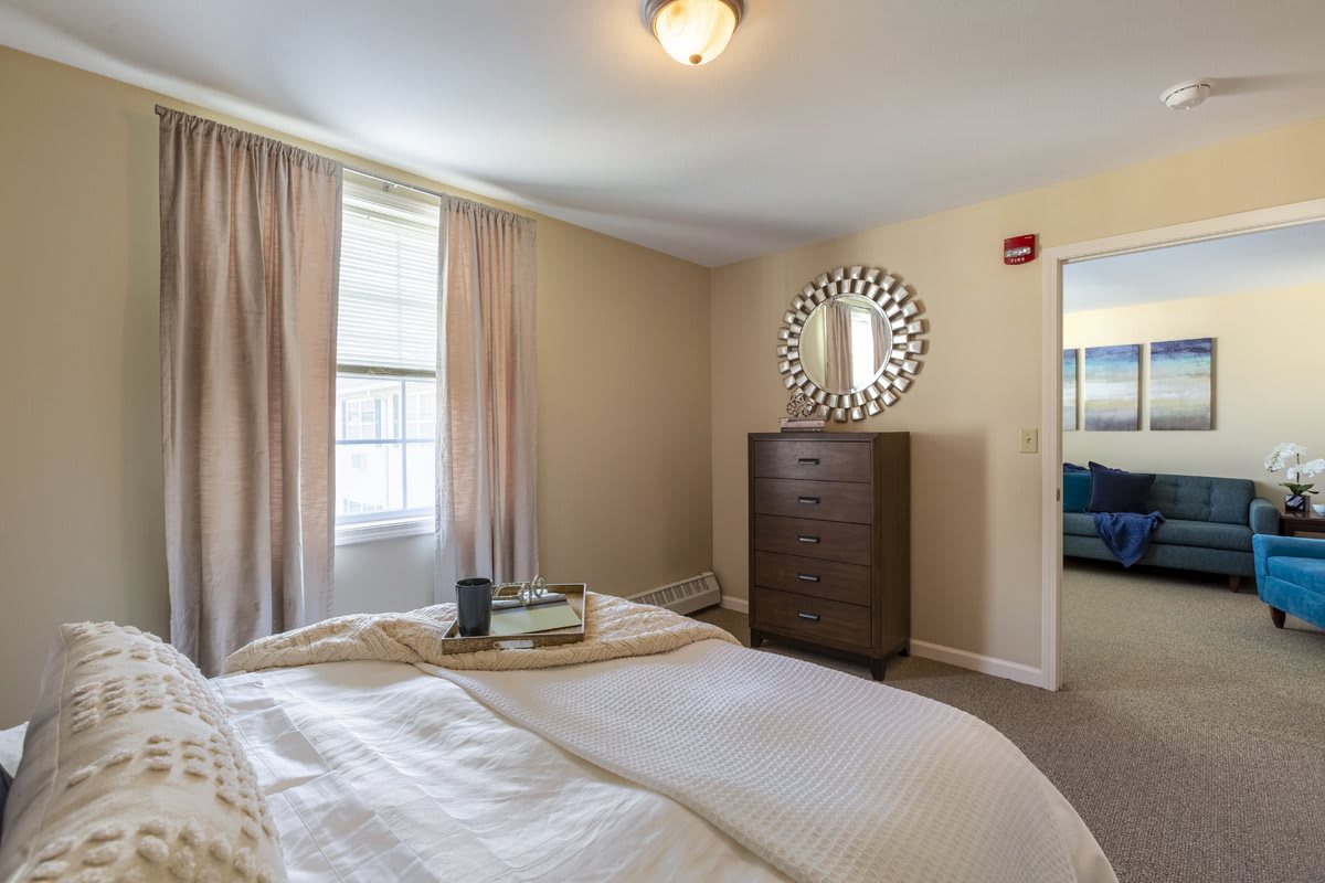 A cozy bedroom with a neatly made bed, a dresser, and a decorative mirror on the wall.