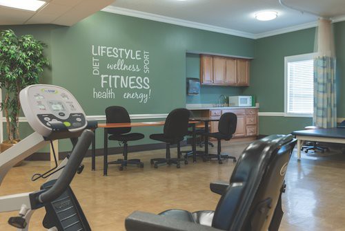 A fitness center room with green walls, motivational wall art, office chairs, and exercise equipment.