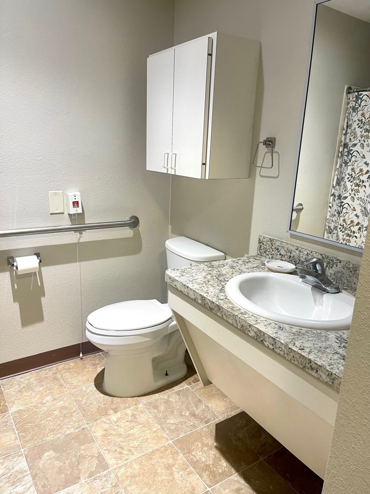 A clean and modern bathroom with a toilet, sink, mirror, and handrail.