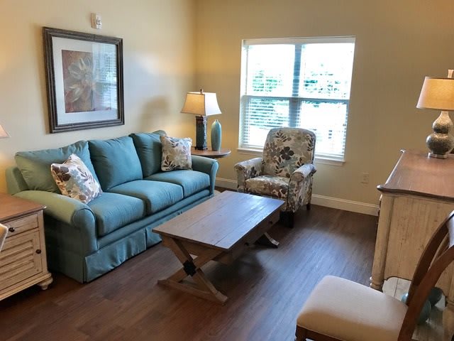A cozy living room with a blue sofa, patterned armchair, wooden coffee table, and a lamp by the window.