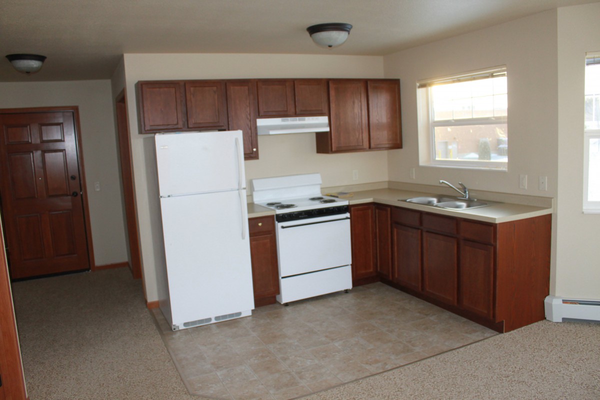 A simple kitchen layout featuring wooden cabinets, a white refrigerator, stove, and a sink under the window.