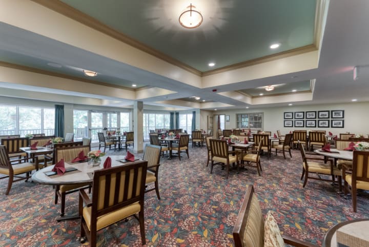 Elegant dining room with neatly arranged tables and chairs, featuring warm lighting and patterned carpet.
