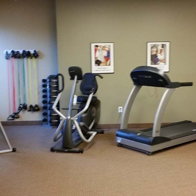 A gym room featuring various exercise equipment including a treadmill, elliptical machine, dumbbells, and resistance bands.