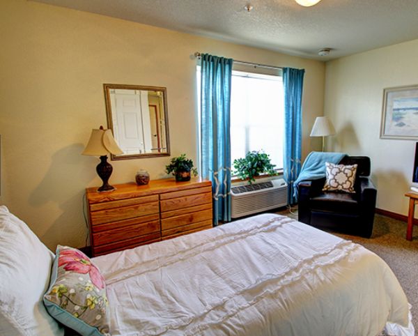 A cozy bedroom with a neatly made bed, a dresser with a mirror, and a comfortable chair by the window.