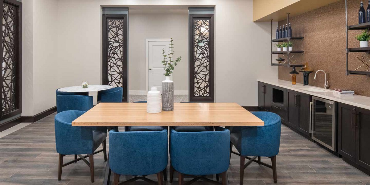 A modern dining area featuring a wooden table, blue chairs, and decorative vases, with ornamental wall panels in the background.