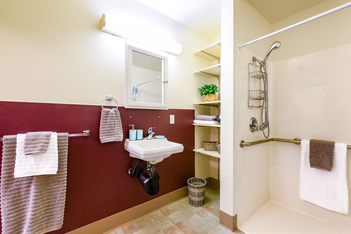 A well-lit bathroom with a sink, shower, and shelving.