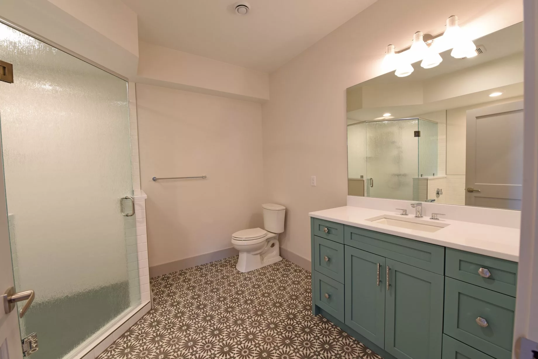 A modern bathroom with a glass shower, toilet, and a vanity with a large mirror.
