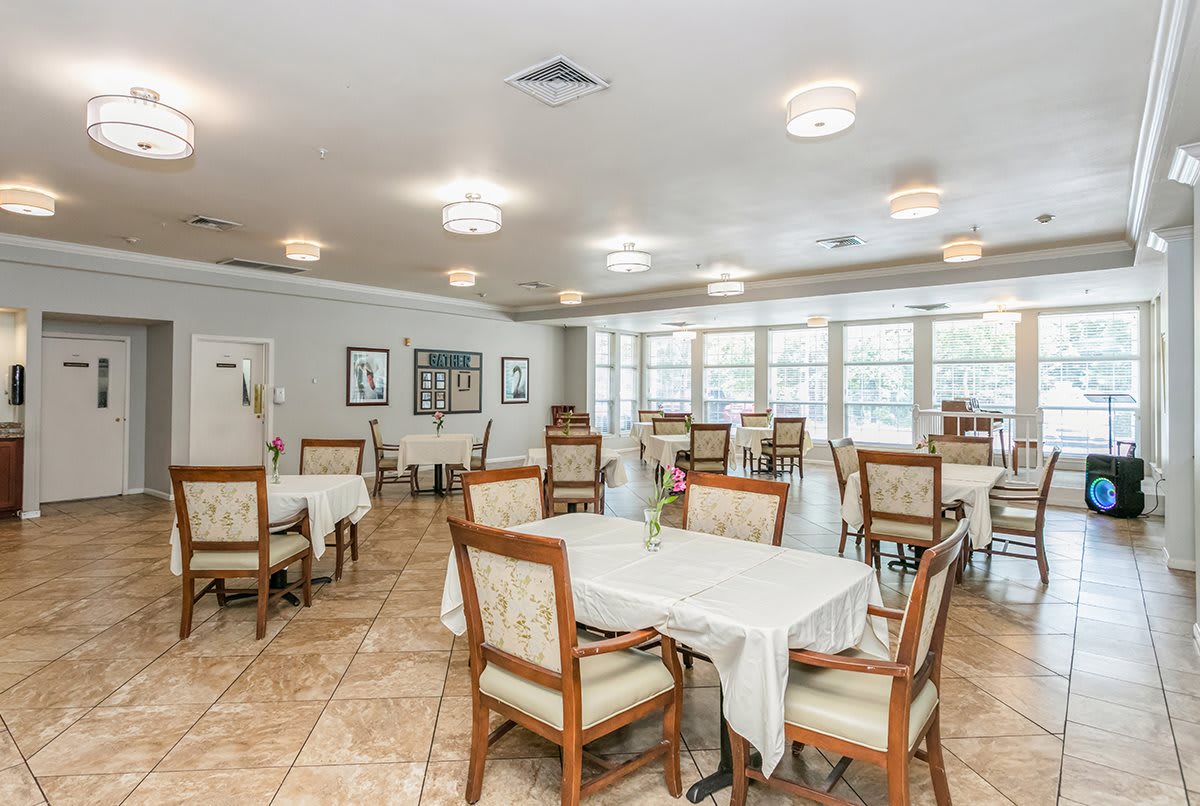 A spacious dining area with neatly arranged tables and chairs, well-lit by overhead lights and natural sunlight through large windows.