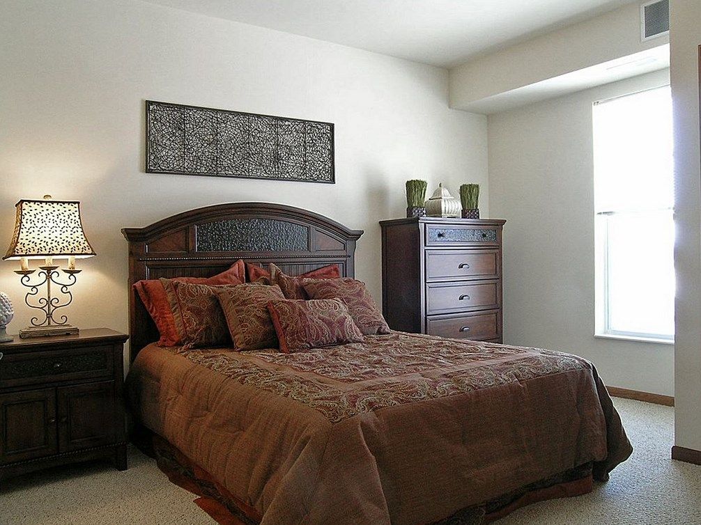 A cozy bedroom with a wooden bed frame, matching dresser, and warm earthy tones.