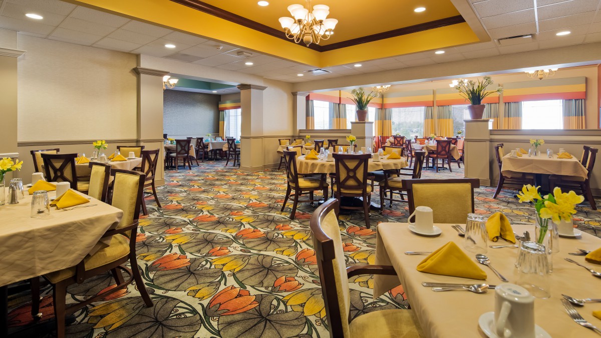 Elegantly decorated dining area with neatly arranged tables, chandeliers, and colorful carpeting.