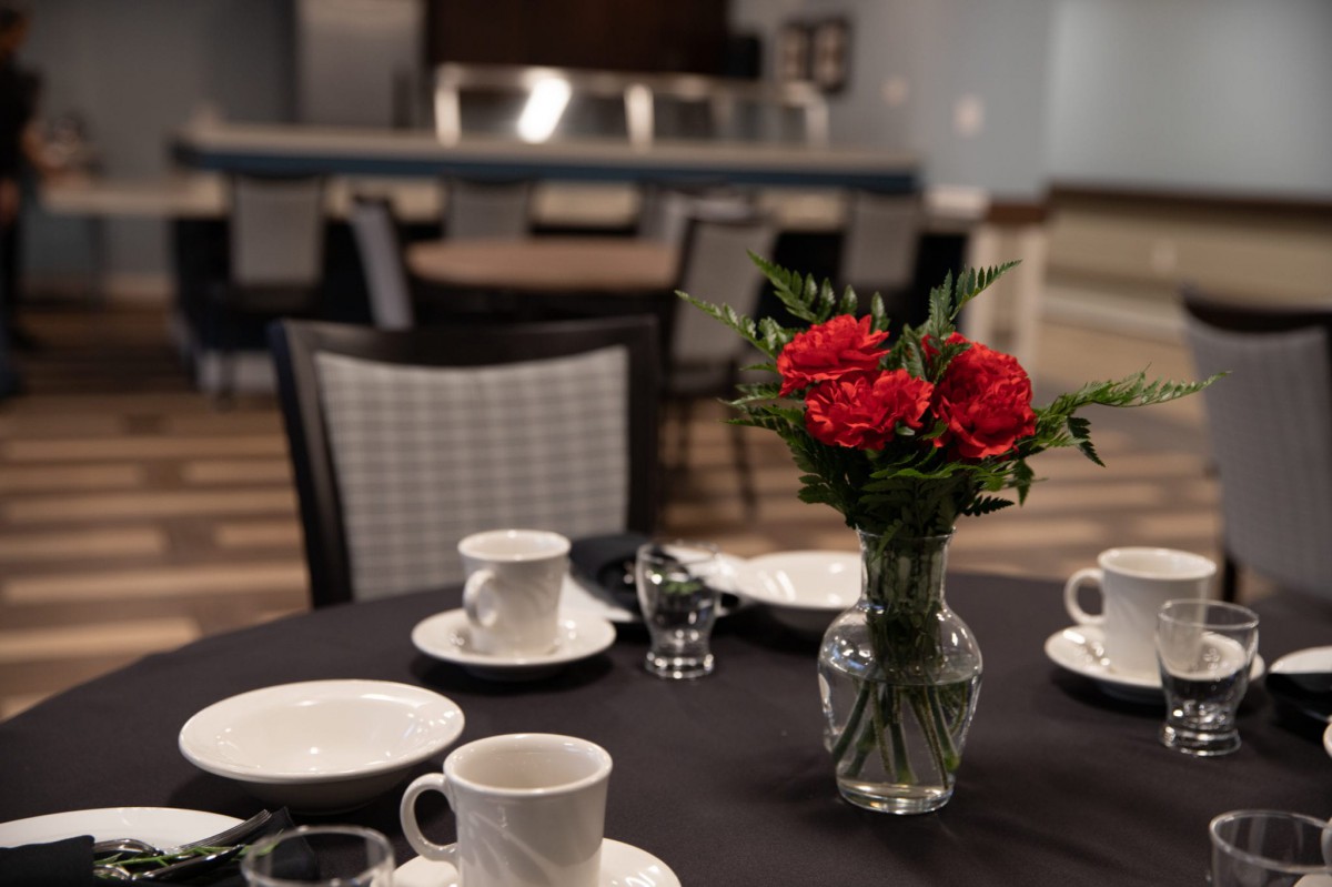 A dining table set with white dishes and a vase of red roses.