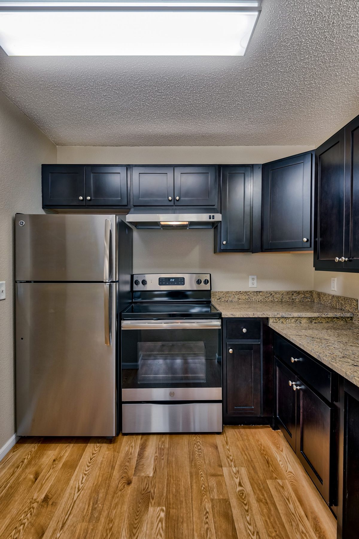 A modern kitchen featuring stainless steel appliances, black cabinets, and granite countertops.