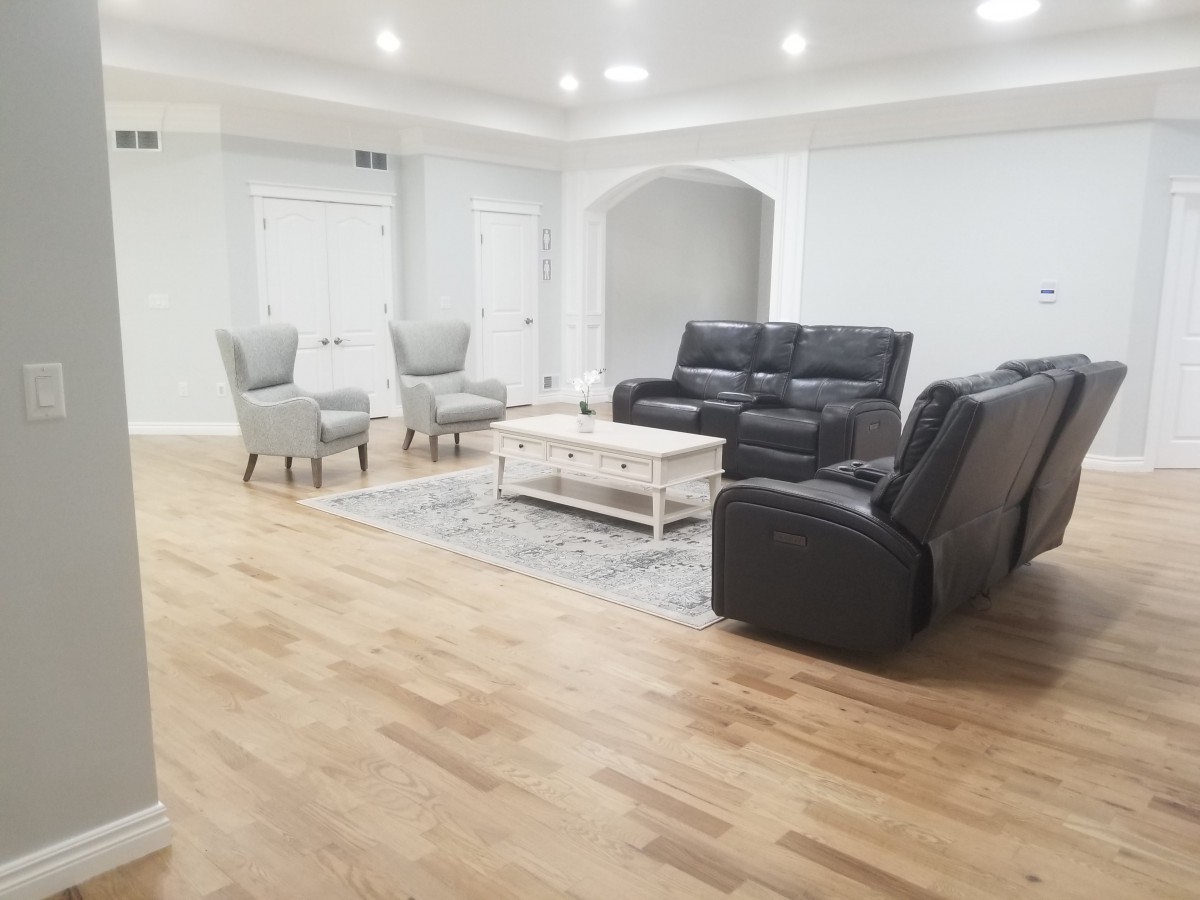 A spacious living room with a minimalist design featuring a black sofa, two grey chairs, a white coffee table, and hardwood flooring.