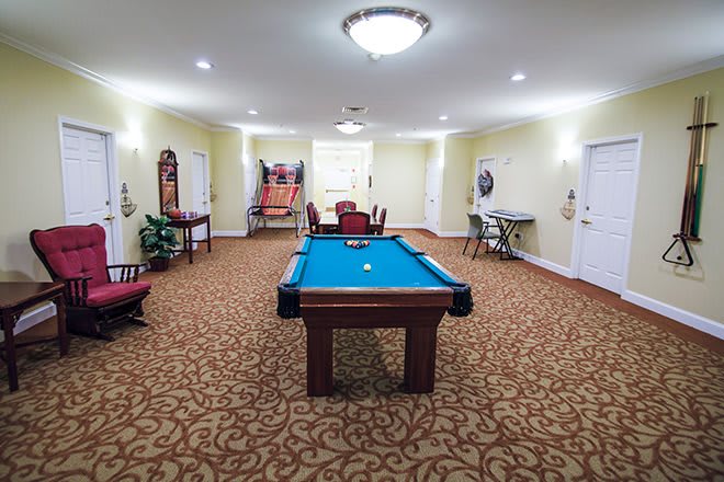 A well-lit game room featuring a pool table and arcade game, set on a carpeted floor.