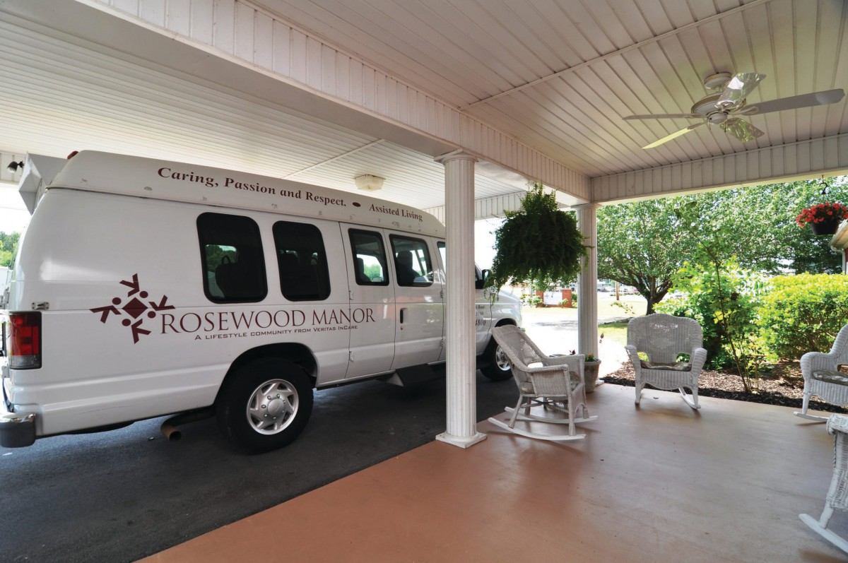 A transport van parked under a covered area with seating and potted plants nearby.