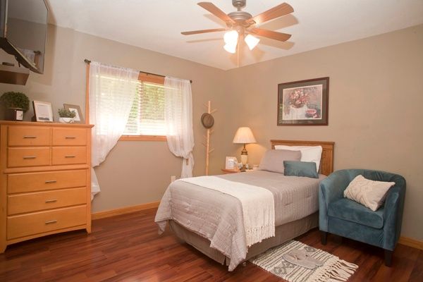 A cozy bedroom with a bed, nightstand, lamp, and a ceiling fan.