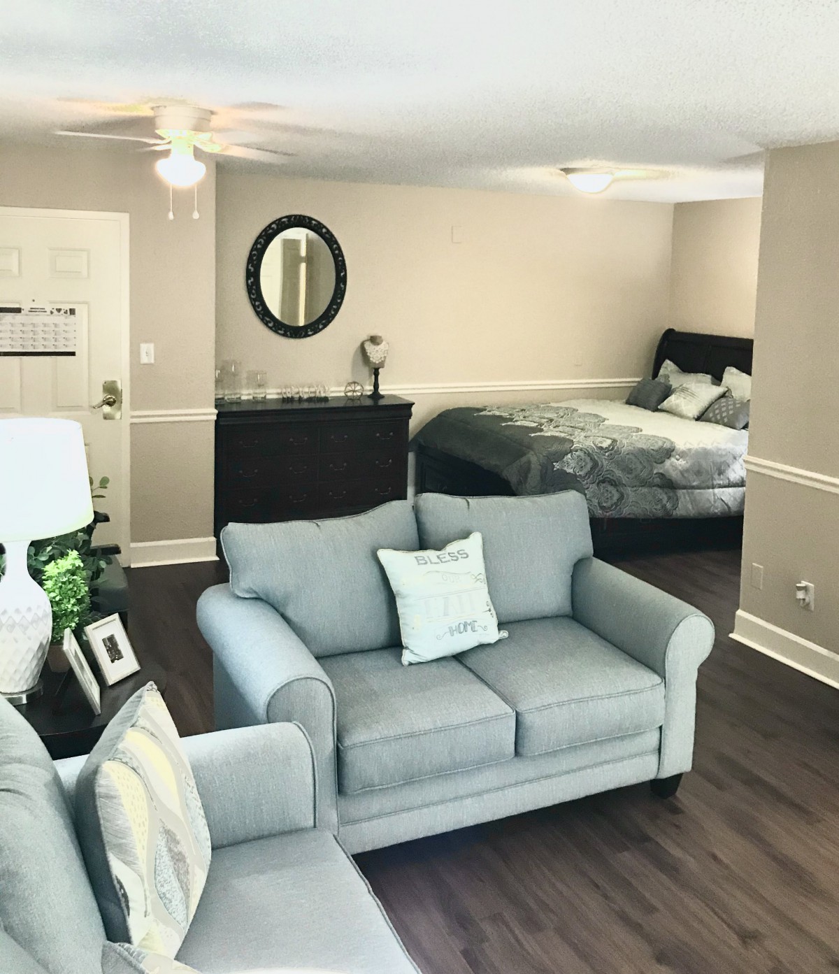 An open-concept living area featuring a cozy gray sofa and a bed in the adjoining space.