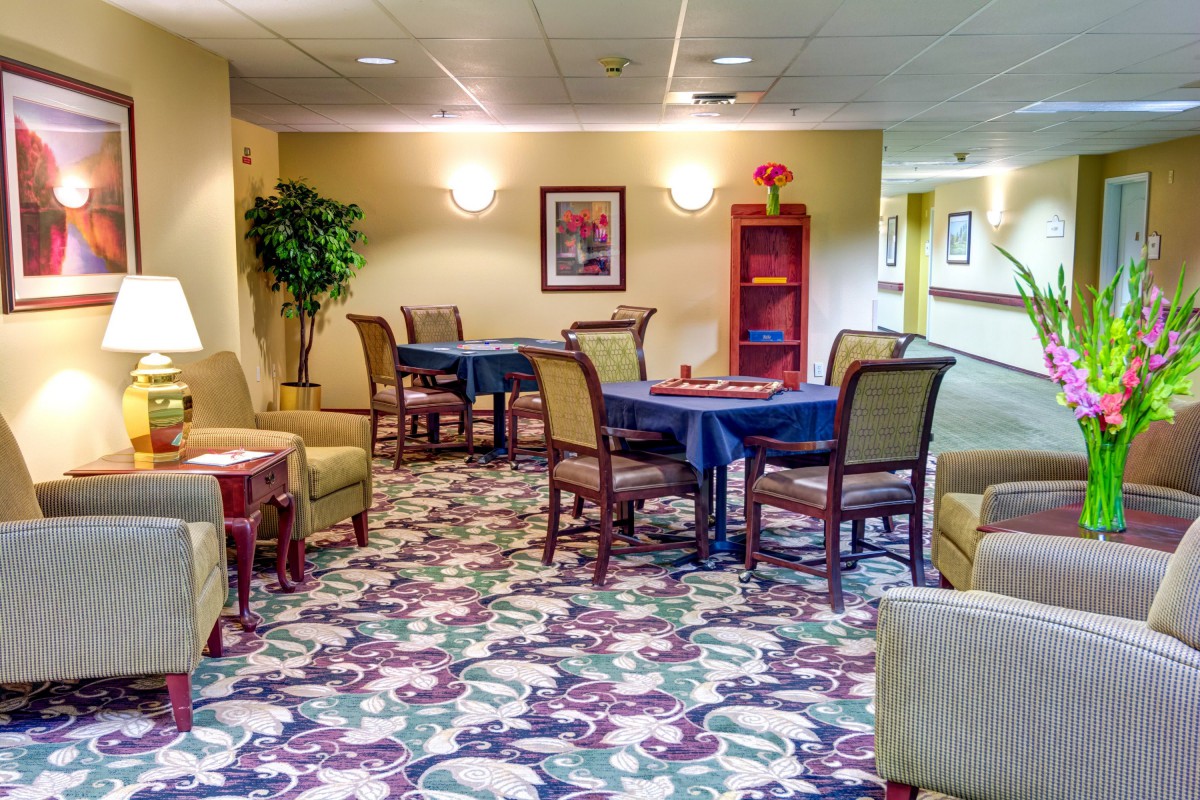 A cozy lounge area with tables, chairs, and vibrant carpeting, accented with decorative plants and wall art.
