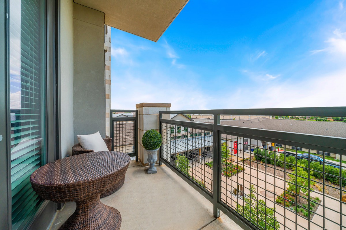 A cozy balcony with wicker furniture, offering a pleasant view under a clear blue sky.