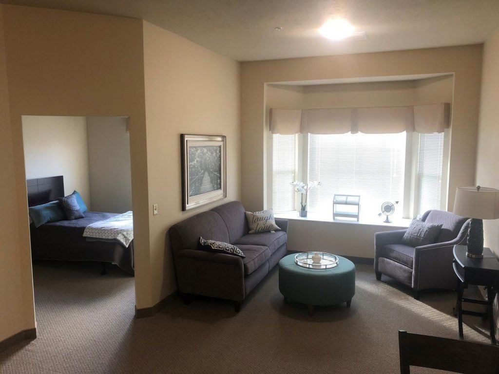 Cozy living room with a sofa, armchair, and coffee table near a window, adjacent to a bedroom.