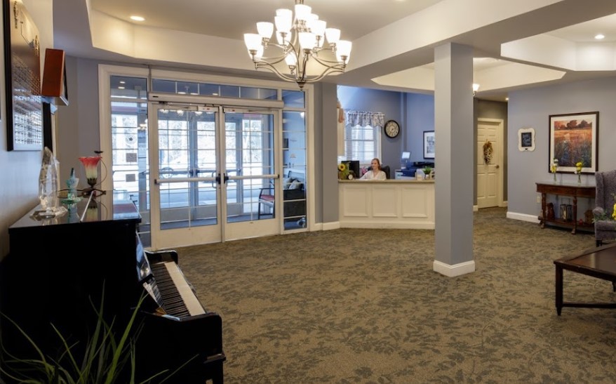 A well-lit lobby with a chandelier, featuring a reception desk and a piano.
