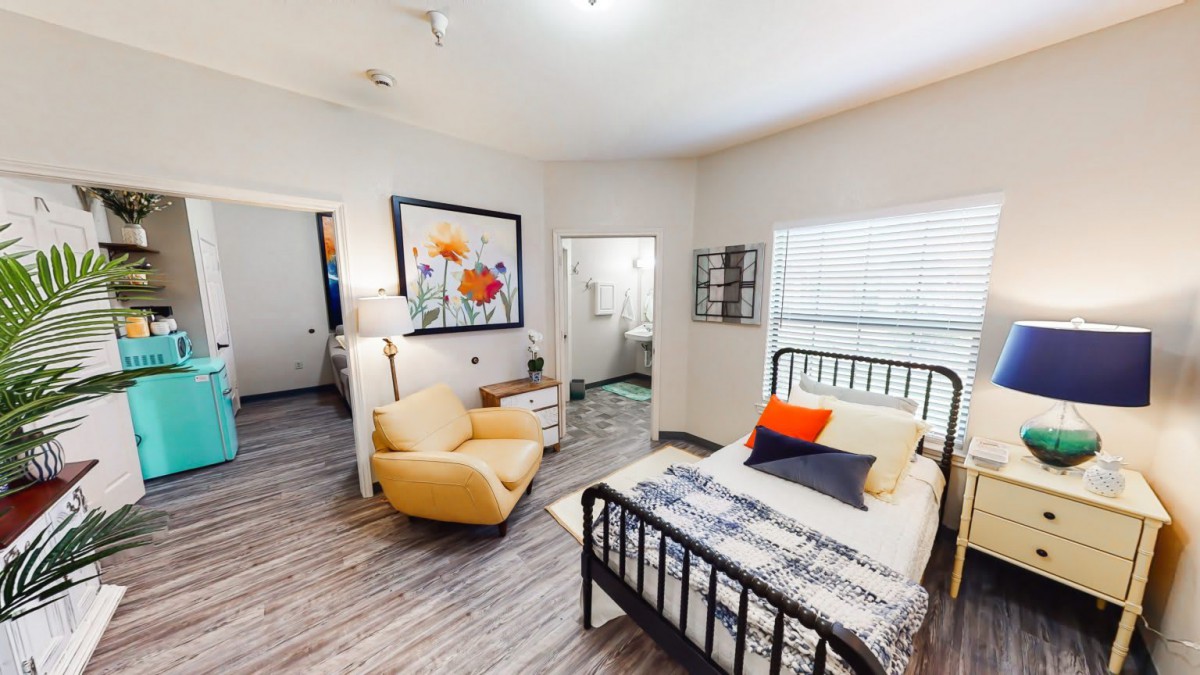 A modern bedroom interior with a bed, a comfortable chair, and colorful wall art.