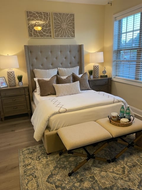 A beautifully decorated bedroom featuring a tufted bed with multiple pillows, bedside tables with lamps, and a bench at the foot of the bed.