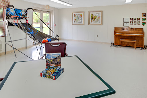 A spacious recreation room featuring a table with puzzles, artworks on the wall, and a piano in the corner.