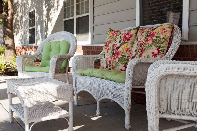 Stylish wicker furniture with floral and green cushions on a sunlit porch.