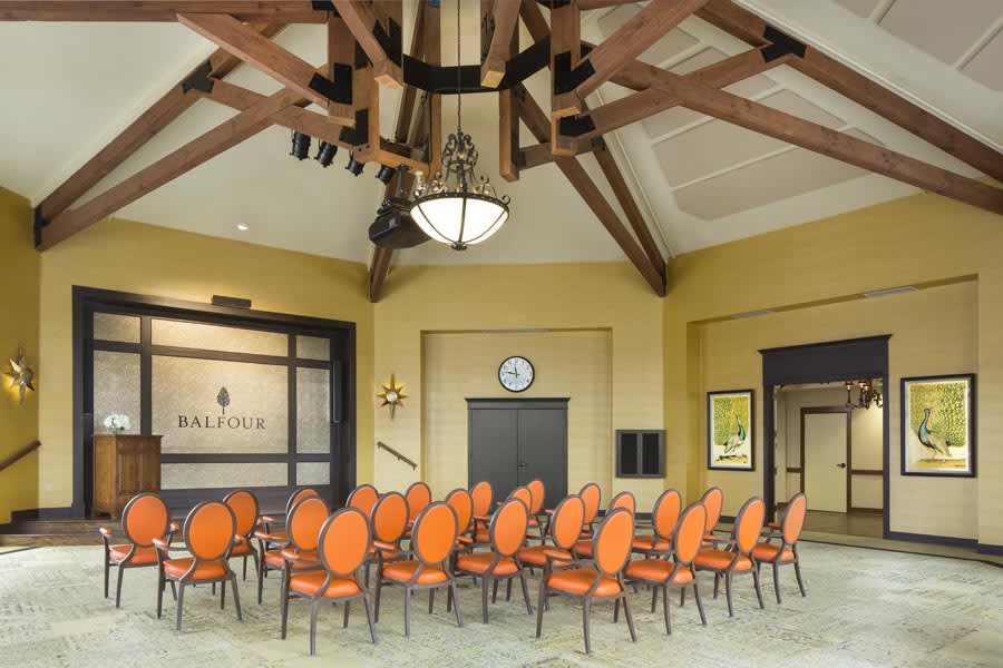 A conference room with orange chairs arranged in a semi-circle, featuring a chandelier and wooden ceiling beams.