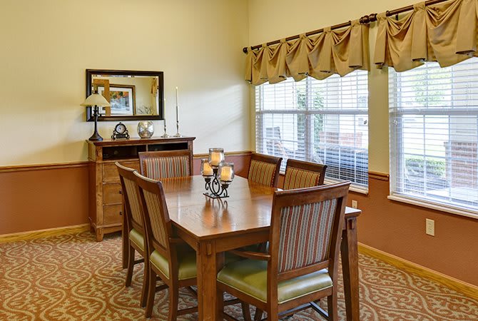 A cozy dining room featuring a wooden table and chairs, complete with decorative elements and a large window.