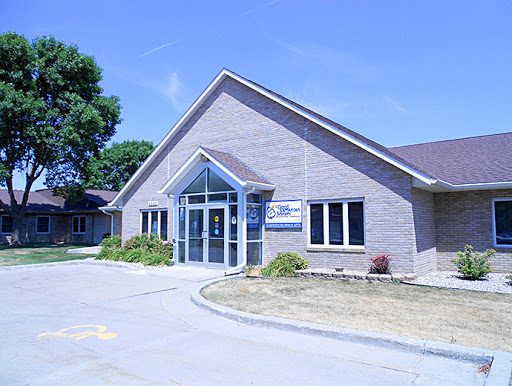 A modern single-story building with large windows and a sloped roof, set against a clear blue sky.
