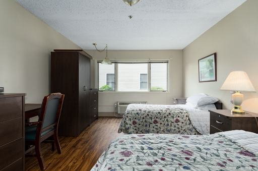 A cozy hotel room featuring two neatly made beds, large windows allowing natural light, and wooden flooring.