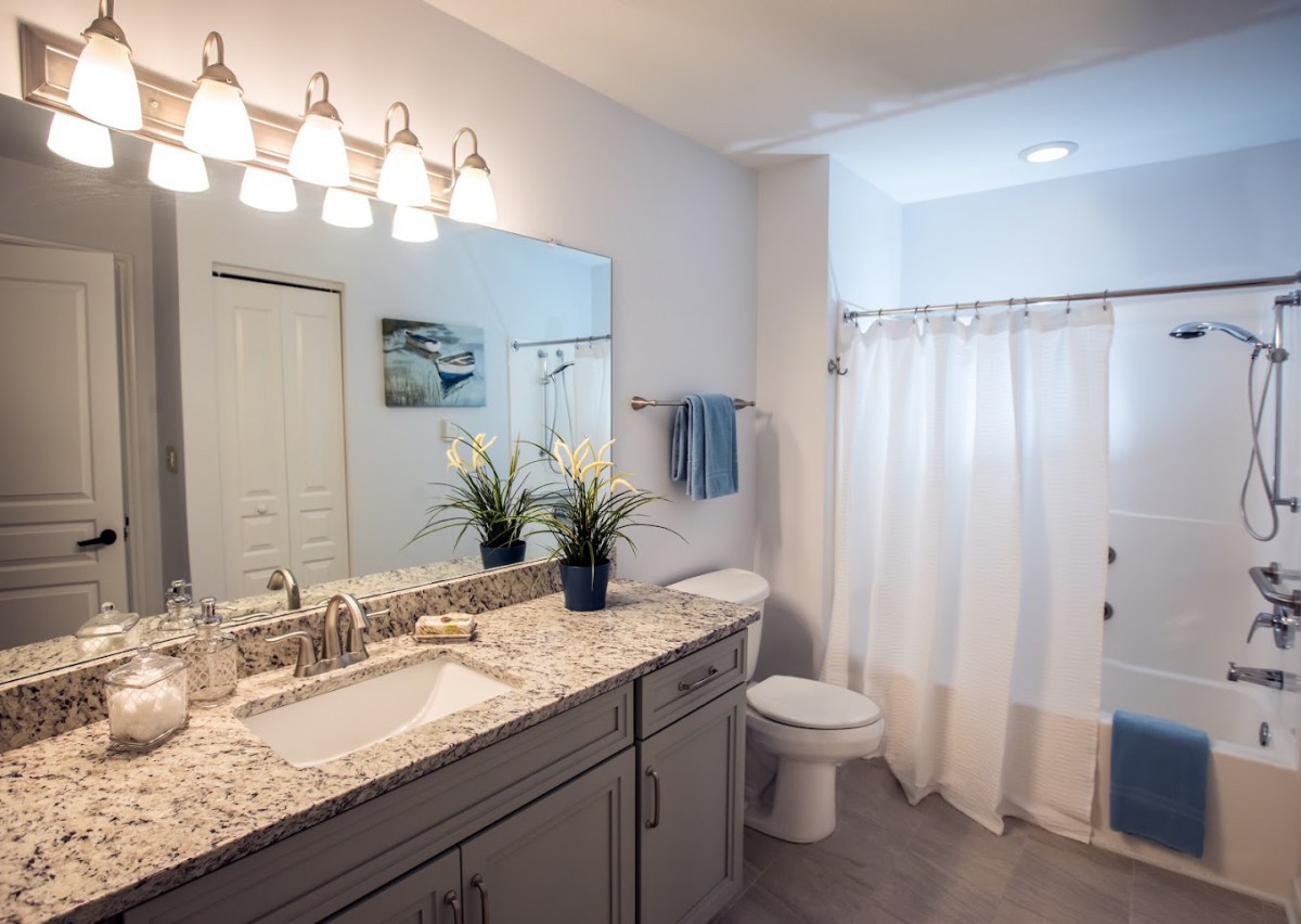 A modern bathroom with a granite countertop vanity, large mirror, and soft lighting.