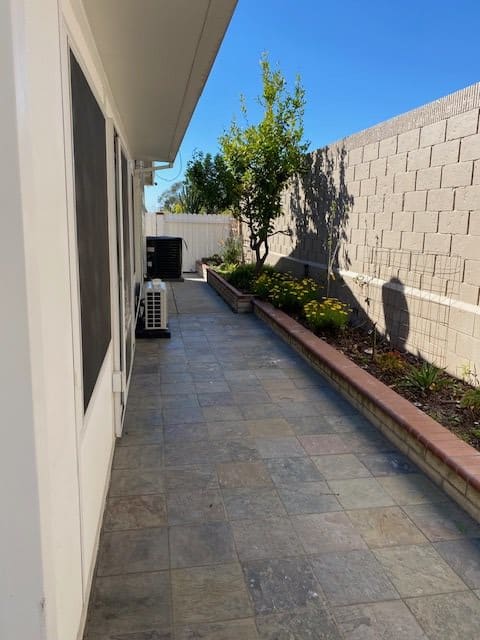 A well-maintained backyard with a paved pathway and landscaped garden along the fence.