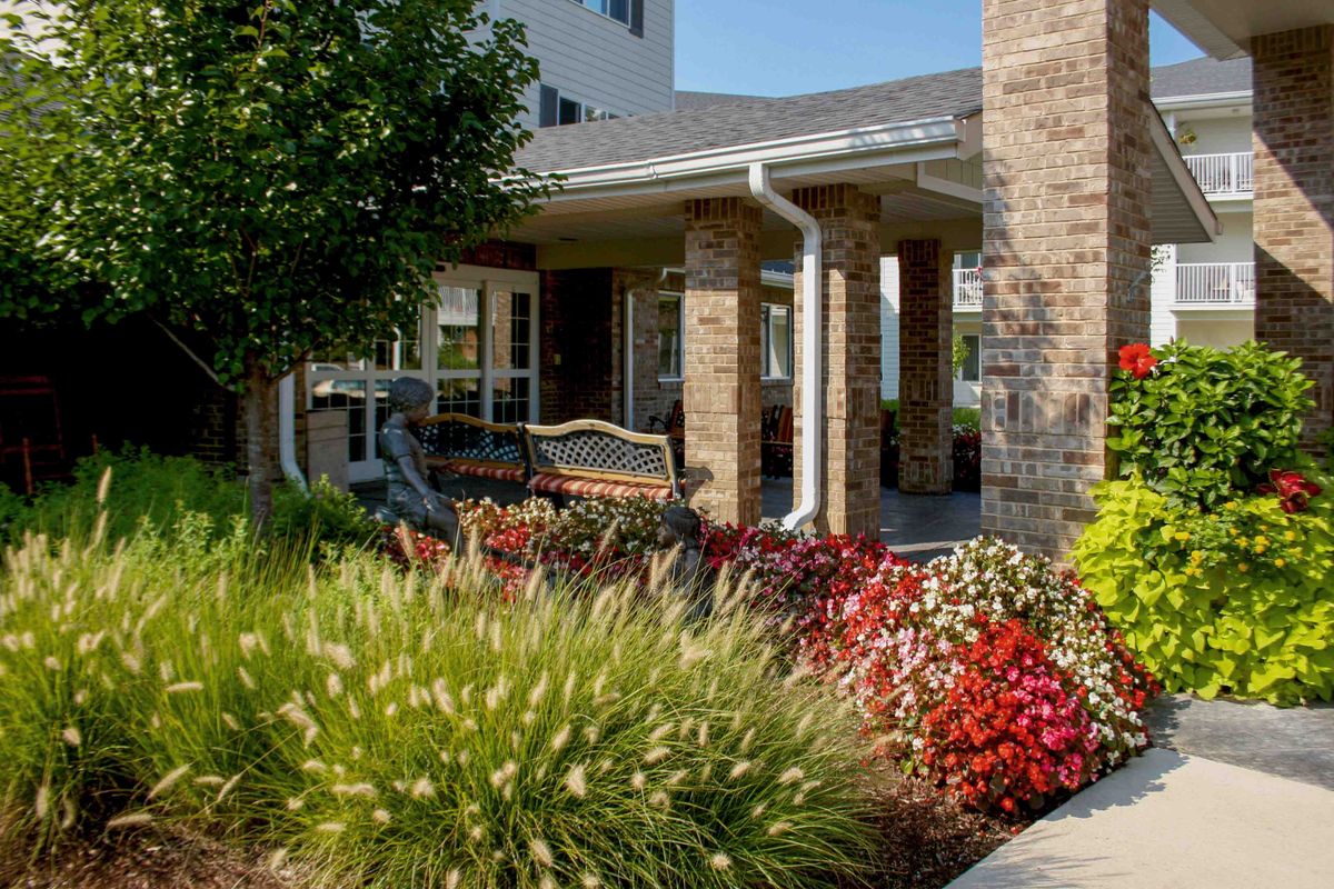 A charming garden area with a bench situated near a building entrance, surrounded by colorful flowers and lush greenery.