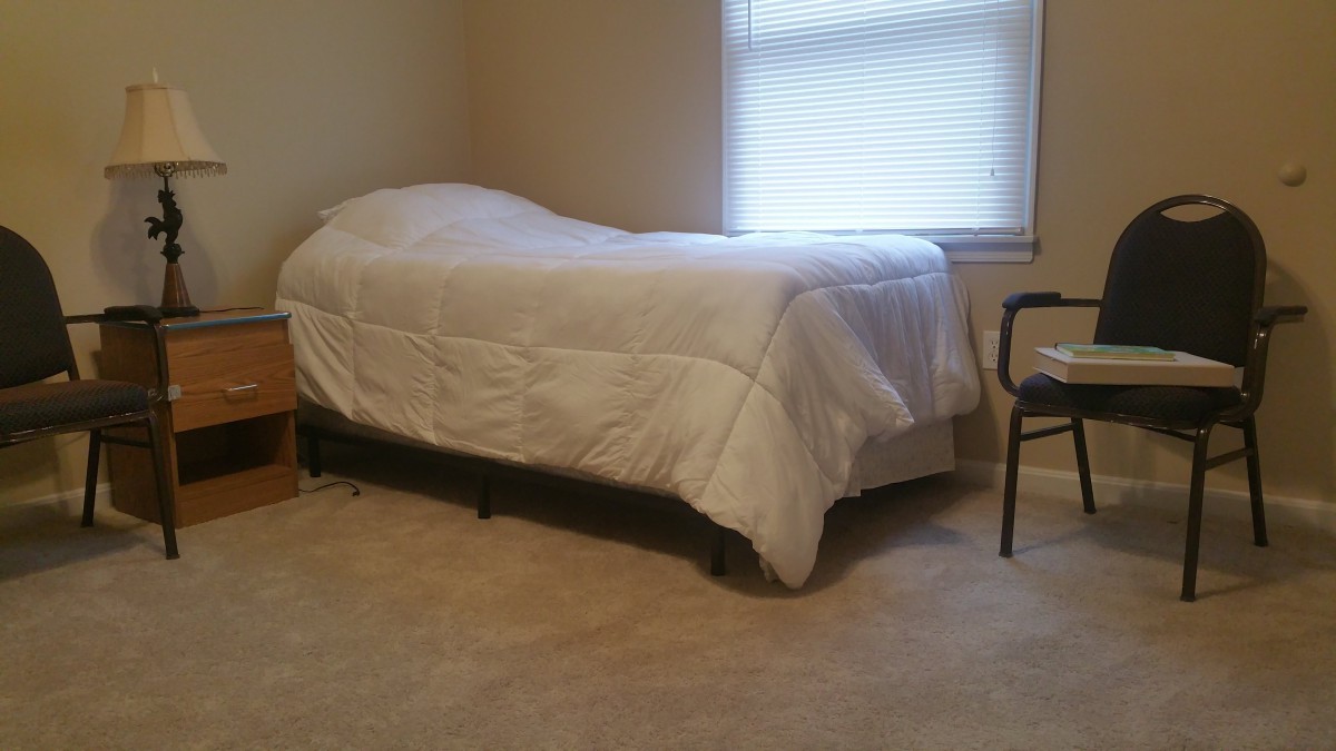 A minimalist bedroom with a single bed and chair next to a window.