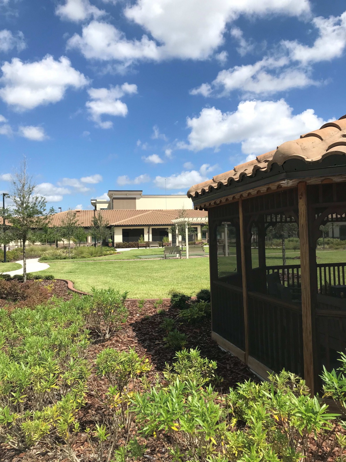 A sunny outdoor landscape featuring a gazebo in front of a large building.