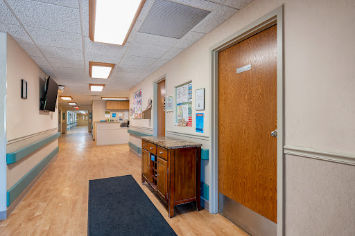 A well-lit hospital corridor featuring wooden doors and a reception area.