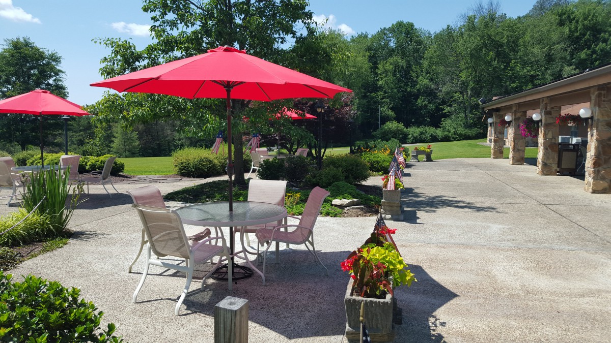 A sunny patio area with a red umbrella and outdoor seating surrounded by lush greenery.