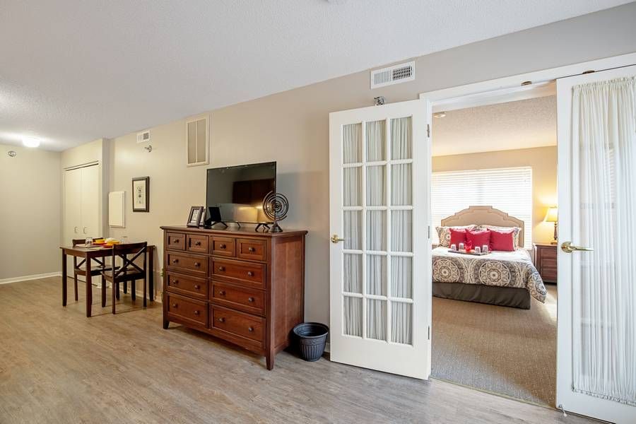 A cozy interior featuring a living room with a dresser and television, leading to a bedroom through French doors.