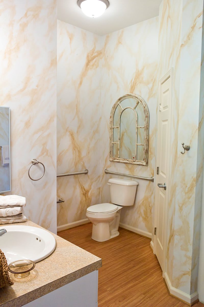 A stylish bathroom with a marble-patterned wall, equipped with a toilet, sink, and mirror.