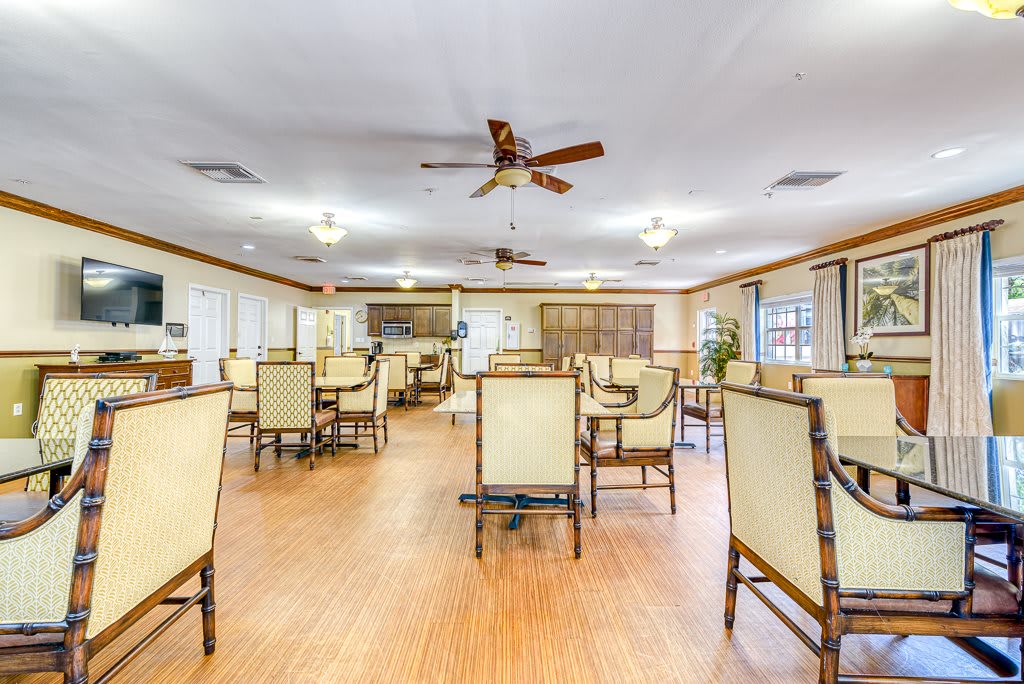 An empty dining room with neatly arranged tables and chairs, featuring ceiling fans and hardwood flooring.