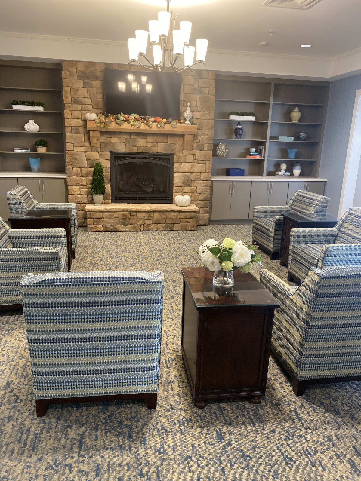 A cozy living room with striped armchairs arranged around a stone fireplace and flanked by built-in bookshelves.