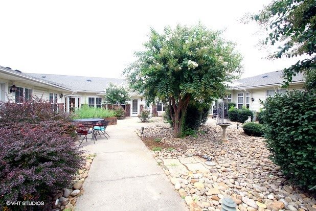 A serene courtyard featuring a paved walkway, lush greenery, and stone landscaping.