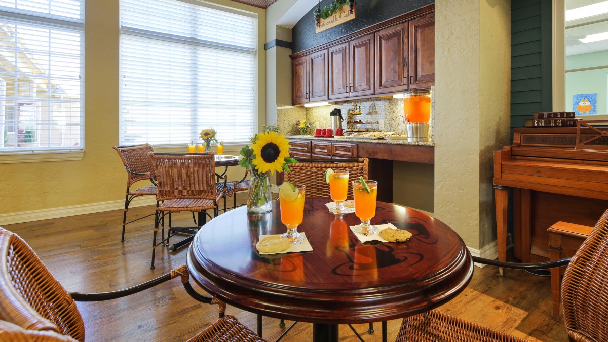 A cozy kitchen with a wooden table set for drinks, featuring sunflowers and wicker chairs.