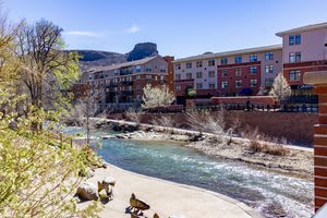 A scenic view of a river flowing through an urban area with buildings and mountains in the background.