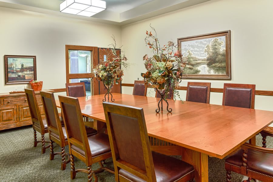 A well-appointed conference room featuring a long meeting table, surrounded by chairs and adorned with floral centerpieces and artwork on the walls.